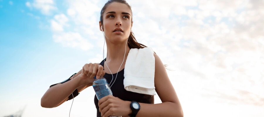 mulher jovem com roupas esportivas se exercitando e segurando uma garrafa de bebida na m