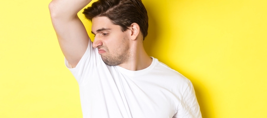 Homem branco suado, cheirando a axila e fazendo careta.